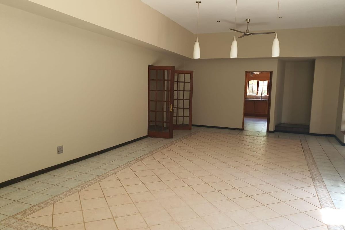 Spacious, empty living area featuring neutral tiled flooring, decorative border inlay, french doors, and modern pendant lighting, leading through to an adjacent kitchen space.