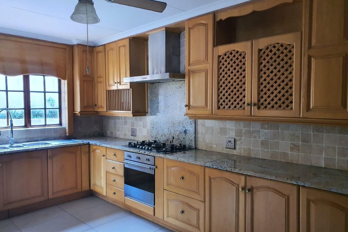 A functional kitchen featuring wooden cabinetry, granite countertops, a gas hob, built-in oven, and a tiled backsplash with a double sink.