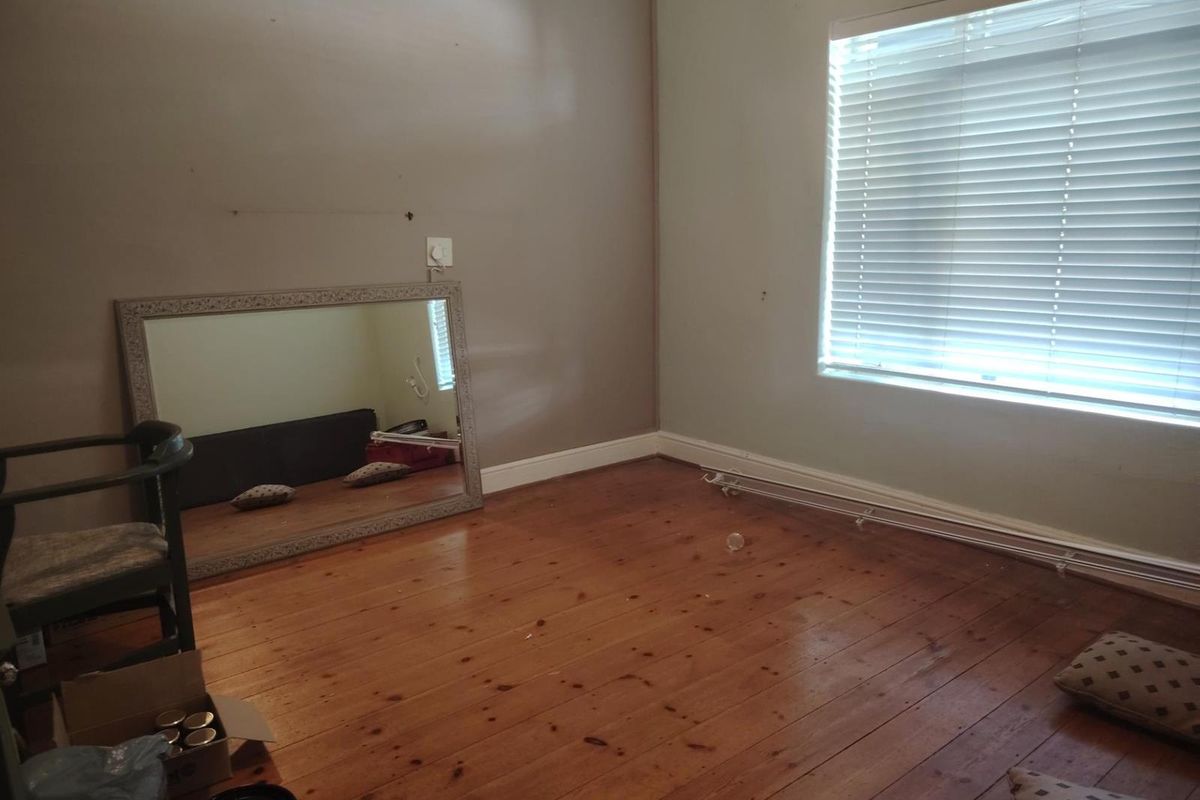 A bedroom featuring polished timber flooring and horizontal window blinds, offering a neutral canvas for interior design.