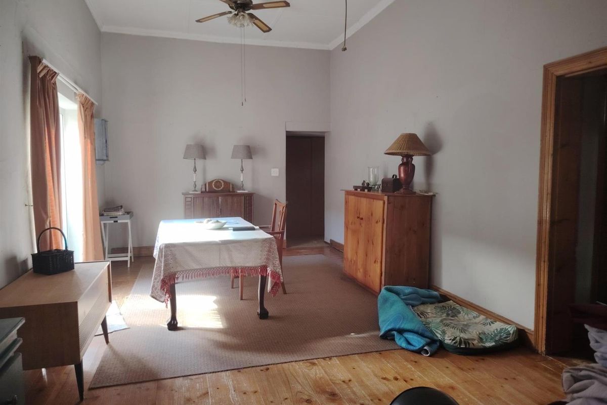 A spacious living area featuring original timber flooring, high ceilings with a mounted fan, and natural light through side windows.