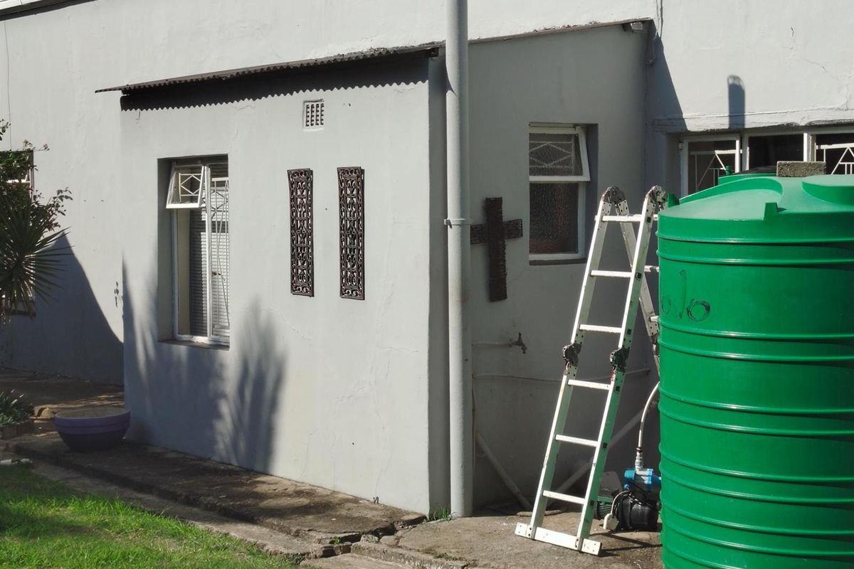 Rear exterior view of the property featuring a painted masonry wall, window security bars, and a large green water storage tank.