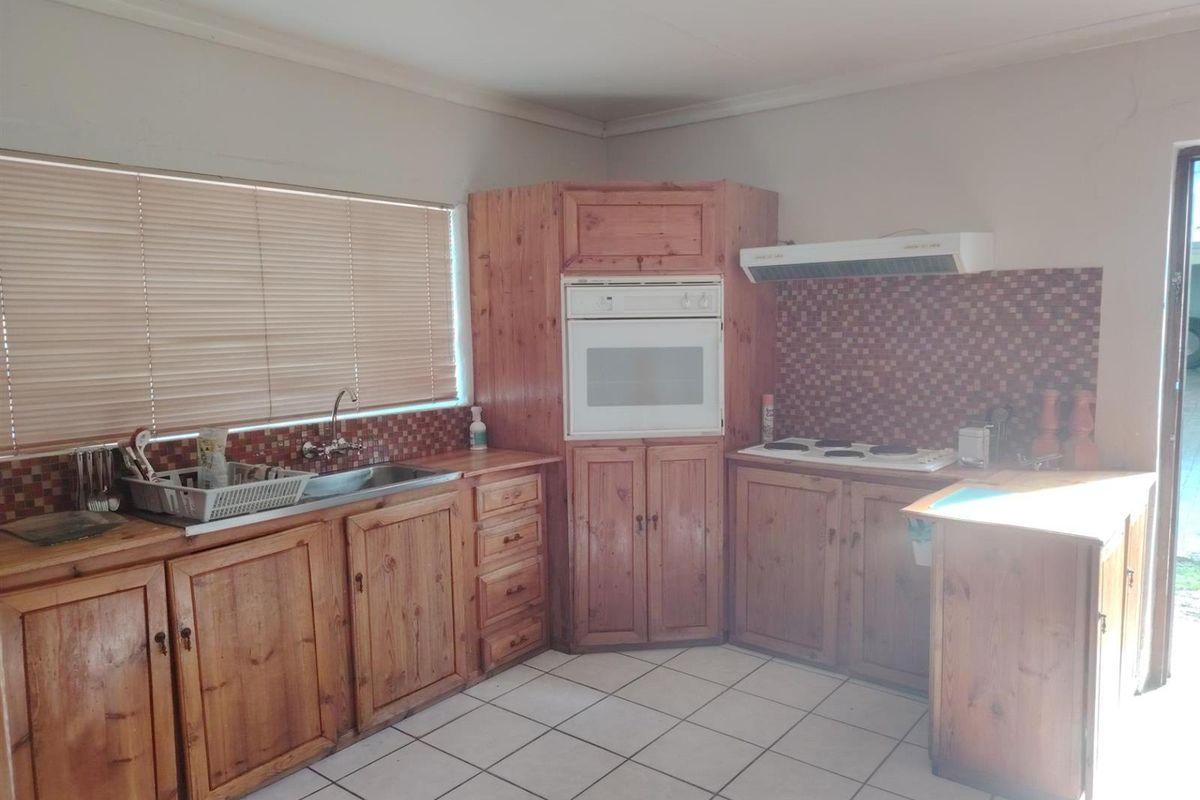 A functional kitchen featuring timber cabinetry, built-in oven, electric cooktop, extractor fan, and tiled flooring with a tiled splashback.