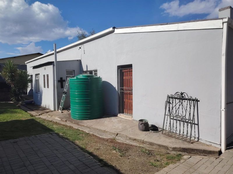 Rear exterior view of the property featuring a paved walkway, a large green water storage tank, and a security gate at the rear entrance.