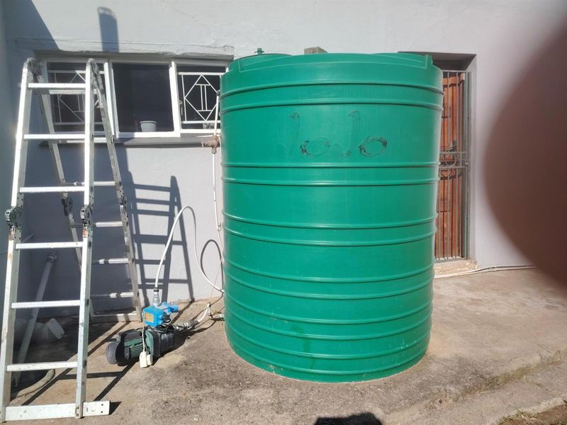 Exterior view showing a green plastic water storage tank with an integrated electric pressure pump system installed on a concrete base.