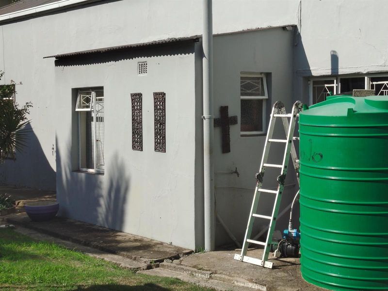 Rear exterior view of the property featuring a painted masonry wall, window security bars, and a large green water storage tank.