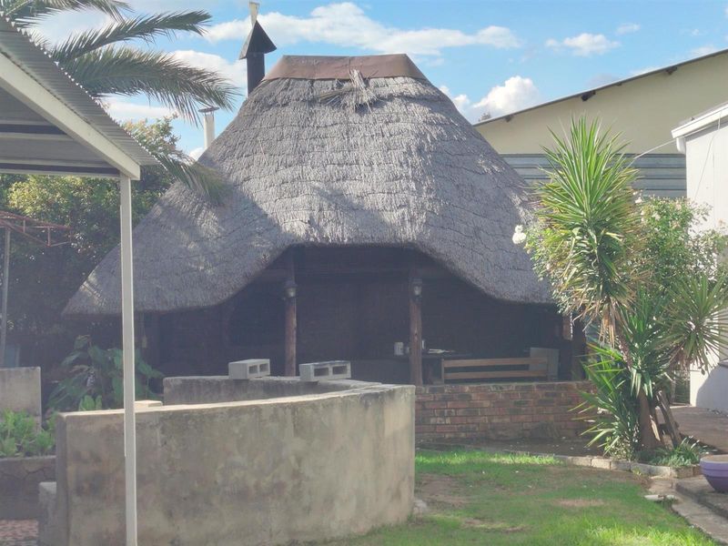 Outdoor thatched lapa area featuring a built-in brick structure, set within a garden space.