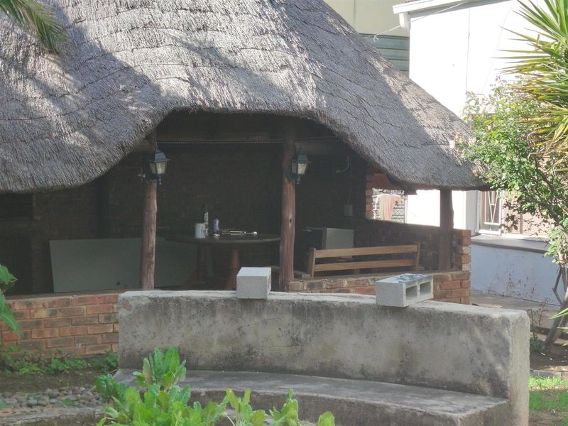 Outdoor thatched lapa entertainment area featuring a brick structure, timber support posts, and a weathered concrete bench in the garden.