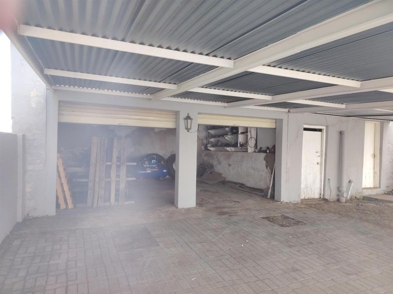 A covered carport area featuring a corrugated metal roof, paved flooring, and access to a garage space with visible structural wear.