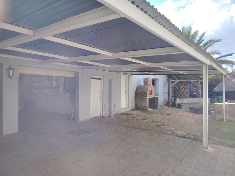 Covered outdoor patio area featuring a built-in brick fireplace, paved flooring, and direct access to the garage and rear garden space.