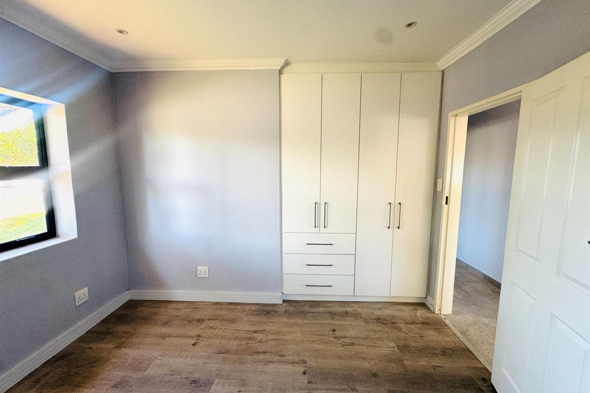 A bright, empty bedroom featuring modern laminate flooring, built-in white cupboards, recessed downlights, and neutral wall finishes.