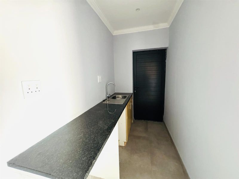 A compact scullery or utility area featuring a granite countertop, stainless steel sink, and base cabinetry, providing functional prep or wash-up space.