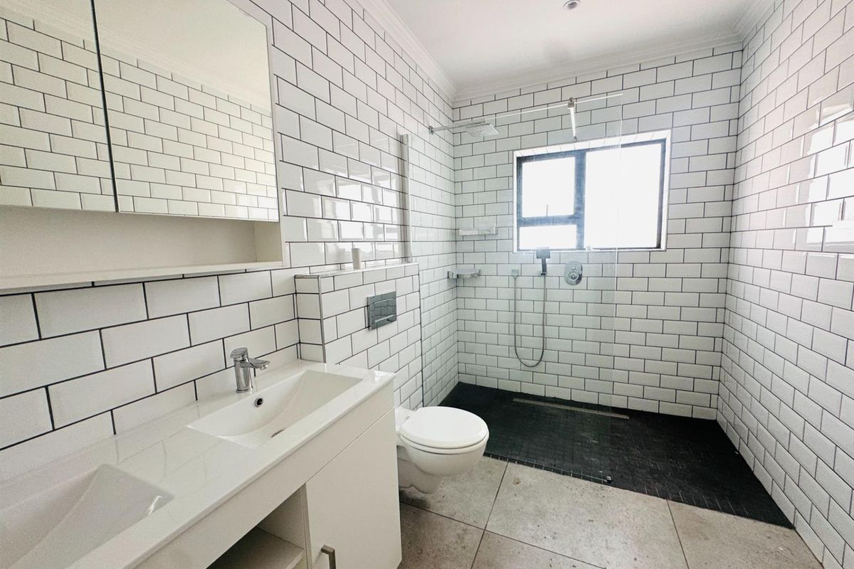 Modern bathroom featuring subway tile walls, a spacious walk-in shower with a rain head, a wall-mounted toilet, and a sleek double vanity.