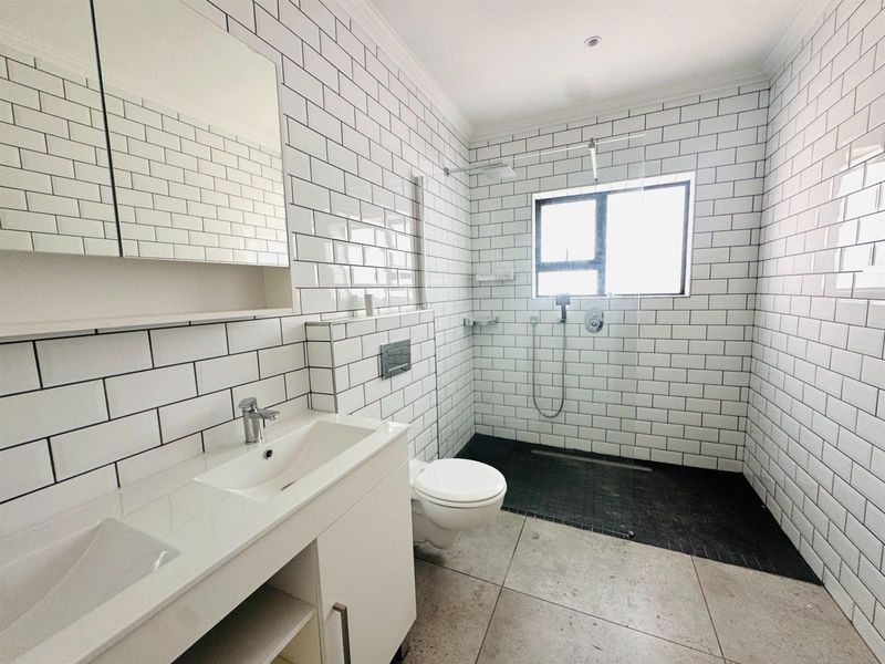 Modern bathroom featuring subway tile walls, a spacious walk-in shower with a rain head, a wall-mounted toilet, and a sleek double vanity.
