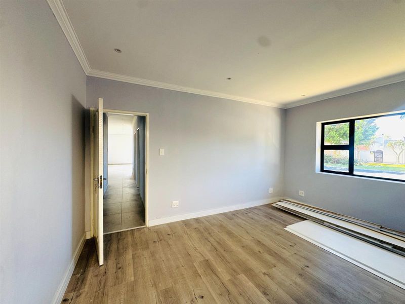 A bright, empty bedroom featuring modern laminate flooring, recessed downlighting, and a black-framed window, offering a clean and neutral canvas.