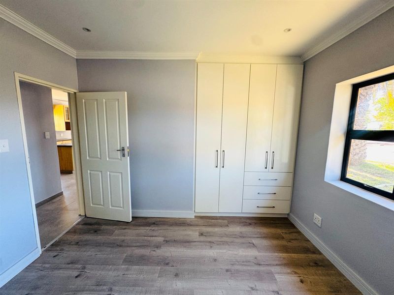 A bright, empty bedroom featuring modern laminate flooring, built-in cupboards, and recessed downlights, offering a clean and neutral space ready for personalization.