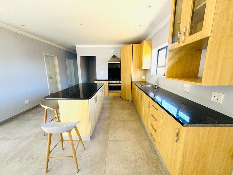Modern kitchen featuring light wood cabinetry, black granite countertops, a central island, and integrated gas stove with extractor fan.