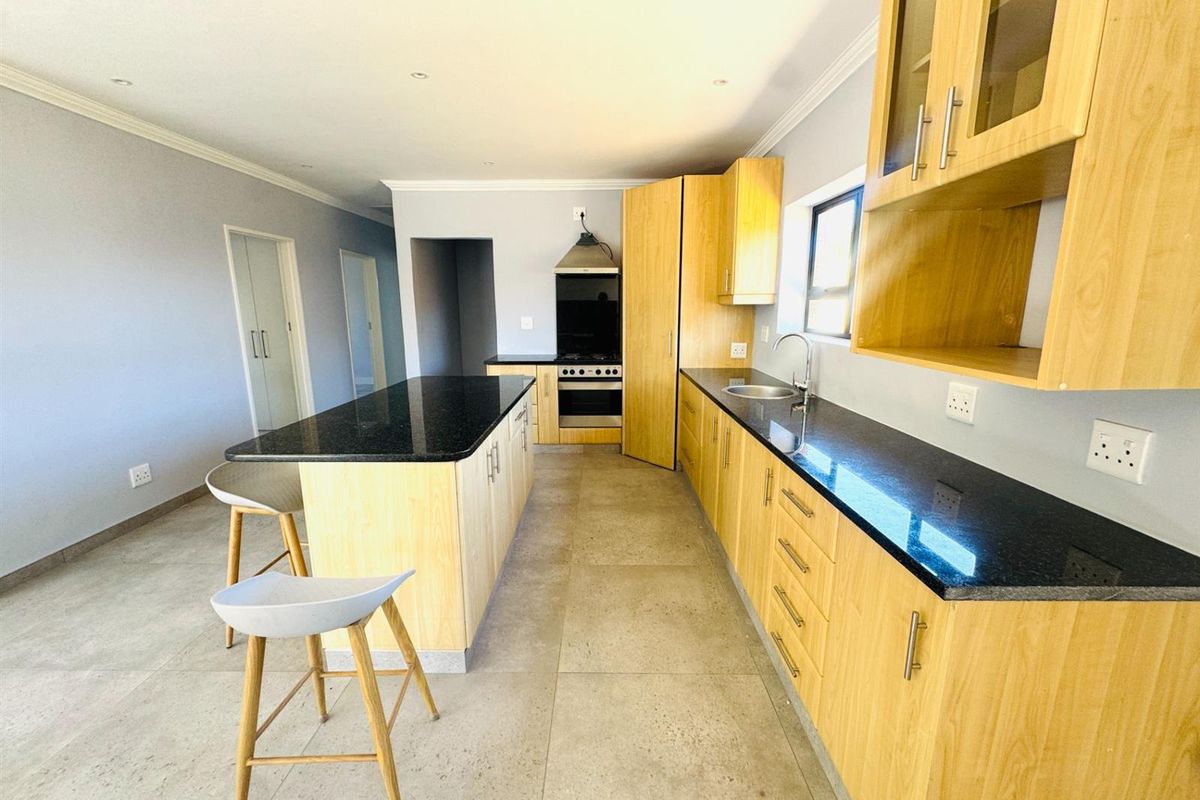 Modern kitchen featuring light wood cabinetry, black granite countertops, a central island, and integrated gas stove with extractor fan.