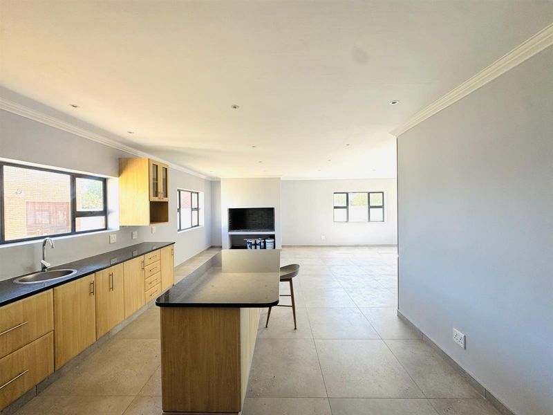 Spacious open-plan kitchen and living area featuring light wood cabinetry, granite countertops, a central island, and a built-in fireplace with neutral tiled flooring.
