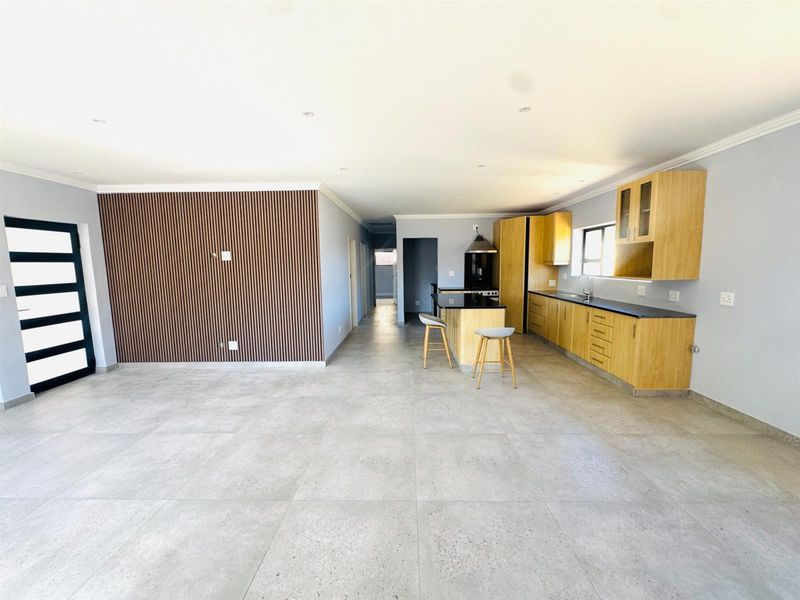 Spacious open-plan living and kitchen area featuring modern timber slat wall detailing, sleek cabinetry, and large format floor tiles throughout.
