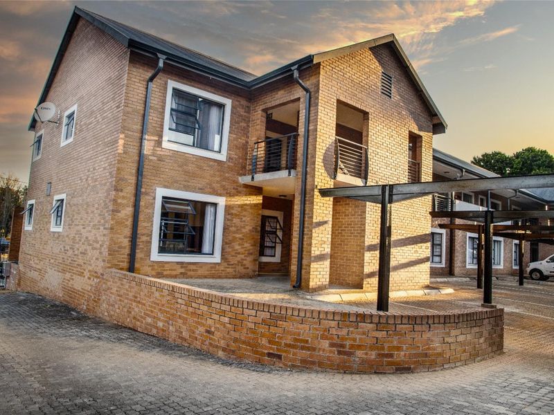 Exterior view of a multi-story townhouse featuring face-brick facade, metal balcony railings, paved driveway, and covered parking structures.