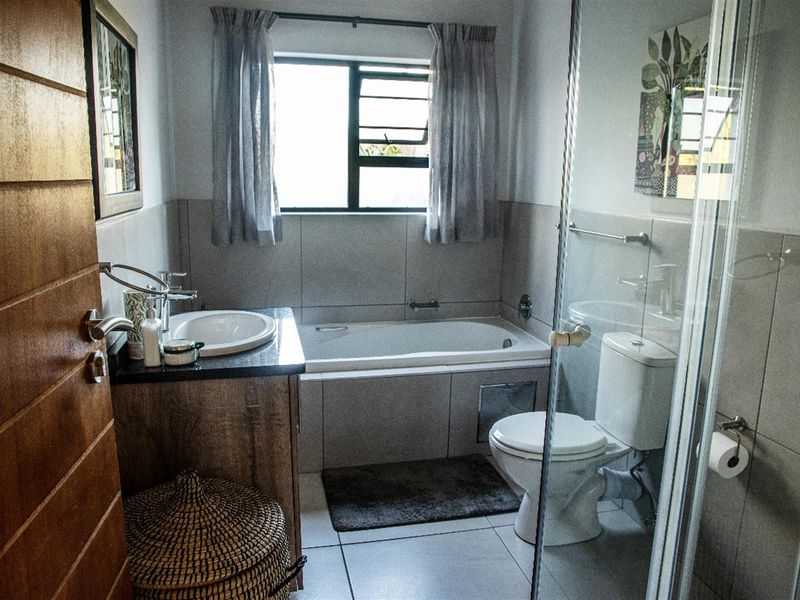 A functional bathroom featuring a built-in bathtub, separate glass-enclosed shower, vanity with basin, and tiled finishes.