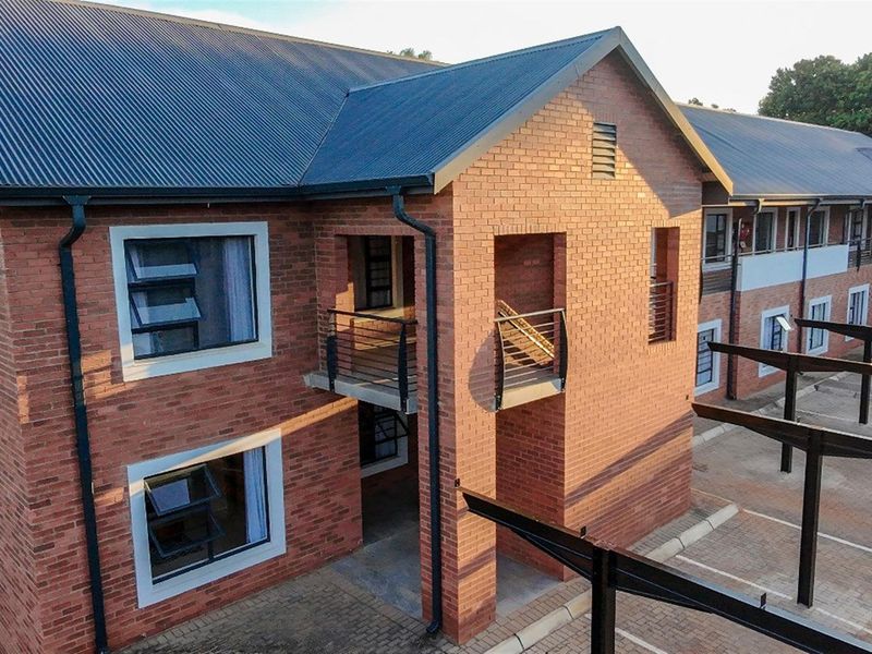 Exterior view of a multi-story brick townhouse complex featuring metal roofing, paved parking areas, and integrated balcony structures.