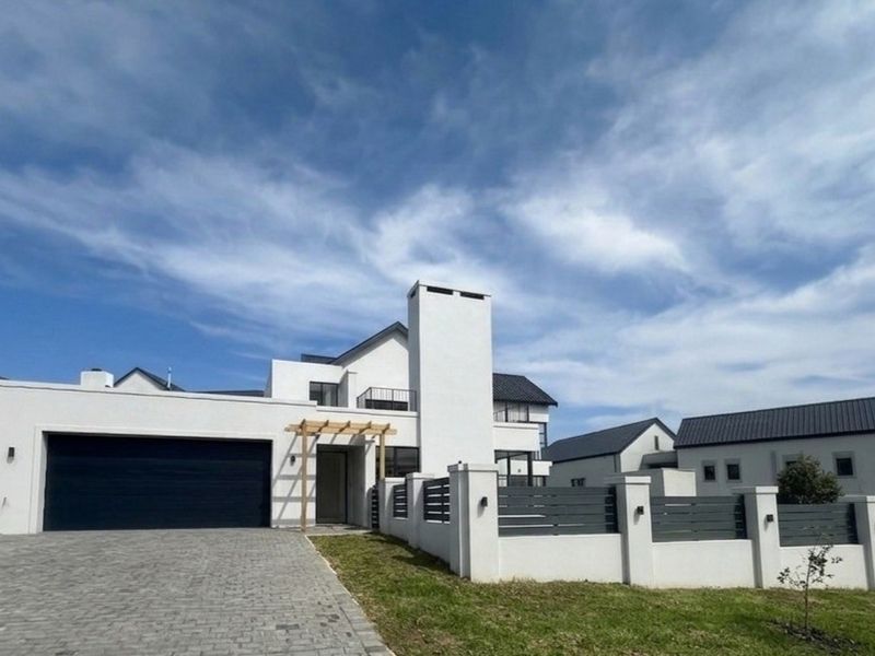 Modern contemporary home featuring a double garage, paved driveway, and secure boundary wall with integrated lighting and a timber pergola entrance.