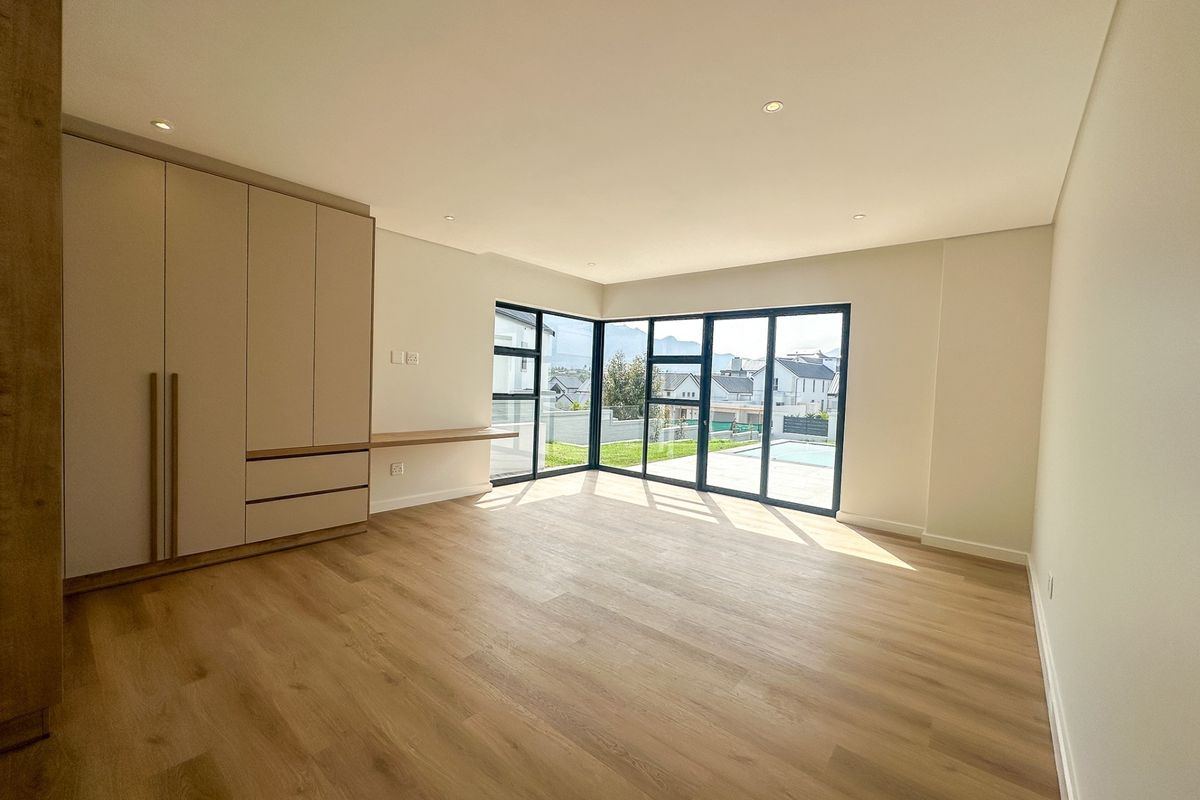 Spacious bedroom featuring modern built-in cupboards, integrated desk, laminate flooring, and large corner windows with sliding doors leading to the pool area.