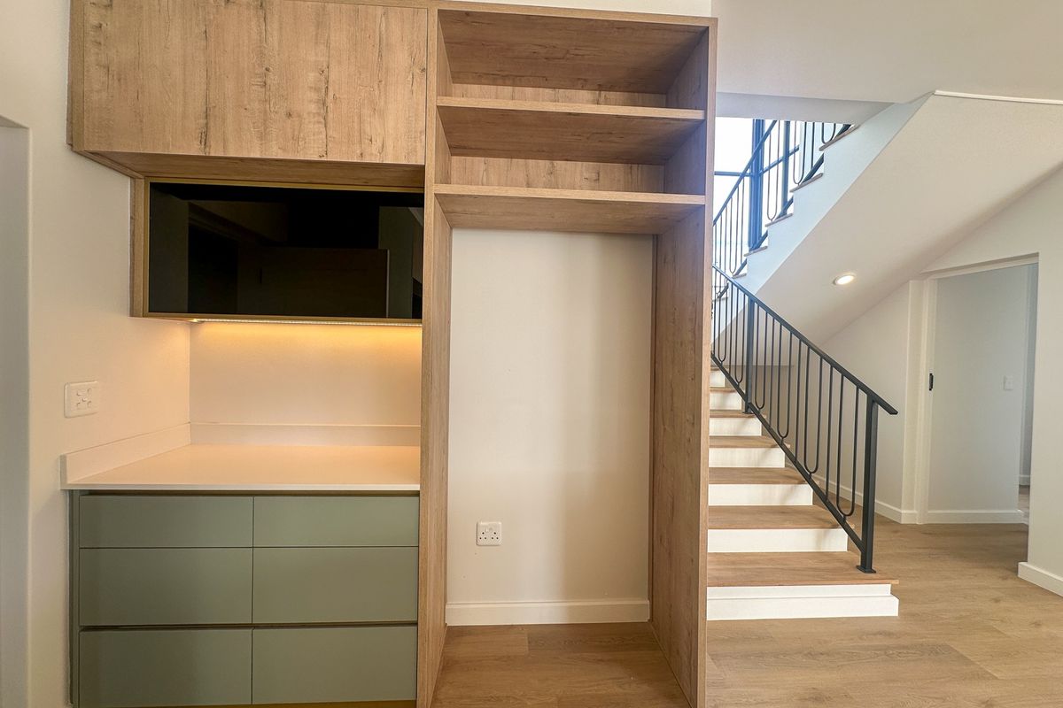 Modern living area featuring custom built-in cabinetry with integrated shelving and a sleek staircase with a contemporary metal balustrade.