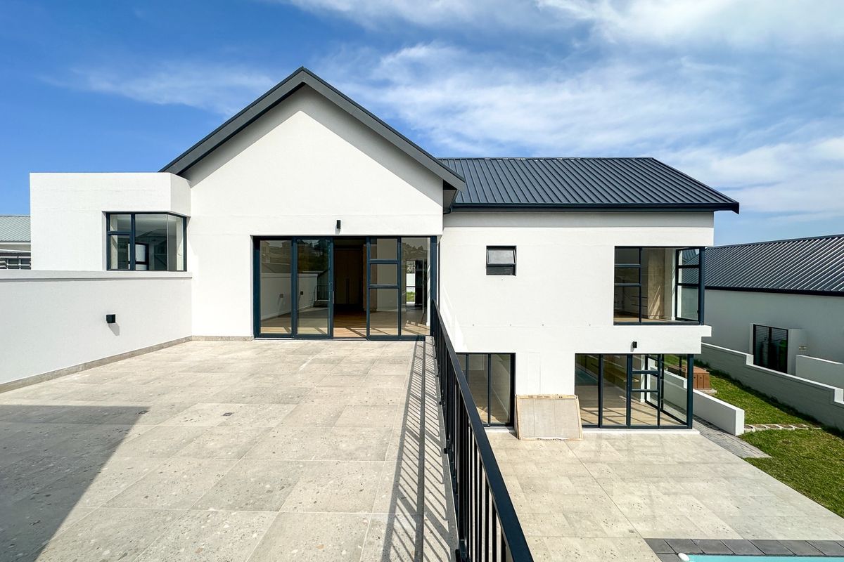 A modern rear elevation featuring a spacious tiled patio, metal roofing, large sliding glass doors, and a swimming pool with a sleek metal balustrade.