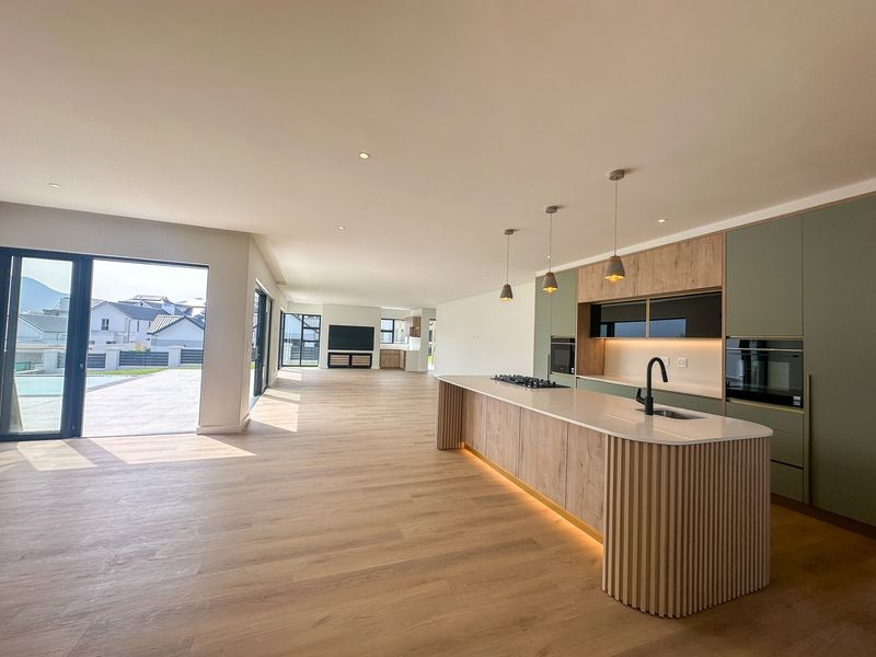 Spacious open-plan living area featuring a modern kitchen with a central island, integrated appliances, and seamless flow to the outdoor patio.