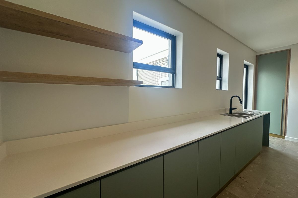 Modern kitchen featuring sleek sage green cabinetry, stone countertops, double sink with black tapware, and floating timber shelving.