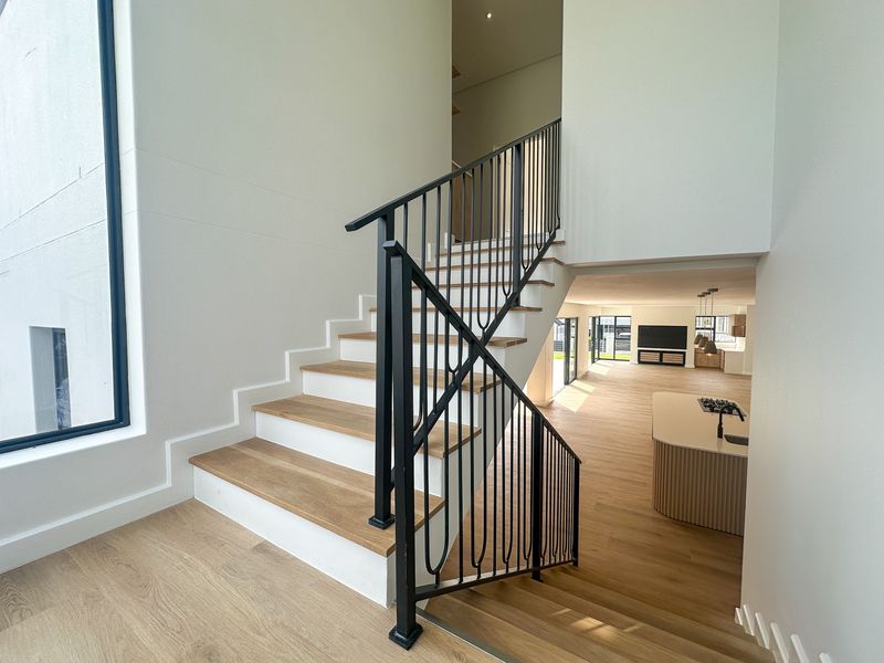 Modern open-plan living area featuring a striking staircase with metal balustrade, timber treads, and a sleek kitchen island with integrated hob.