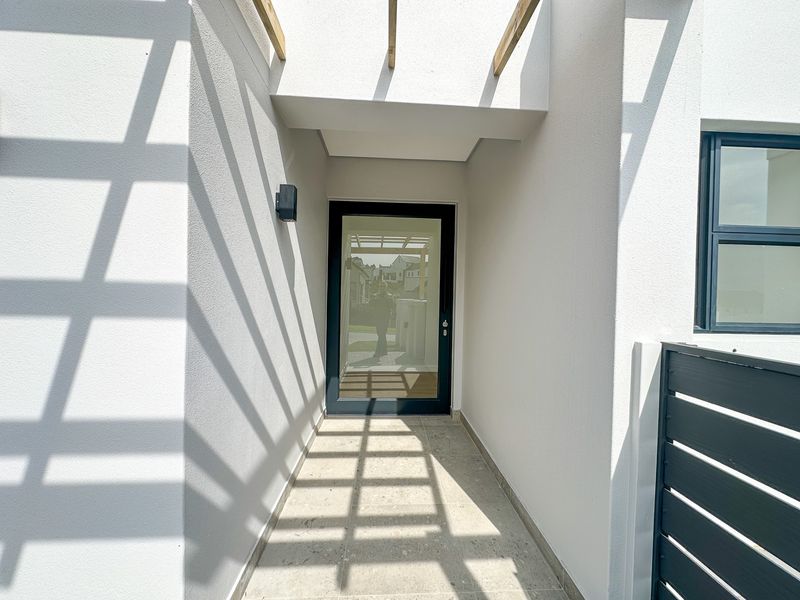 A modern, clean entrance area featuring a timber pergola, tiled flooring, and a contemporary glass-panelled front door.