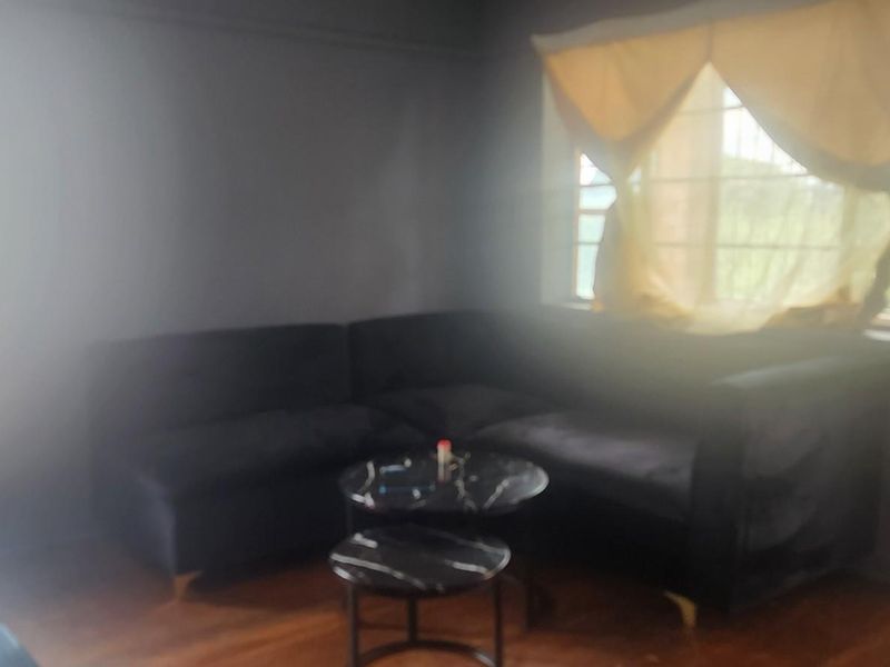 A living room featuring hardwood flooring and large windows with security bars, offering natural light.