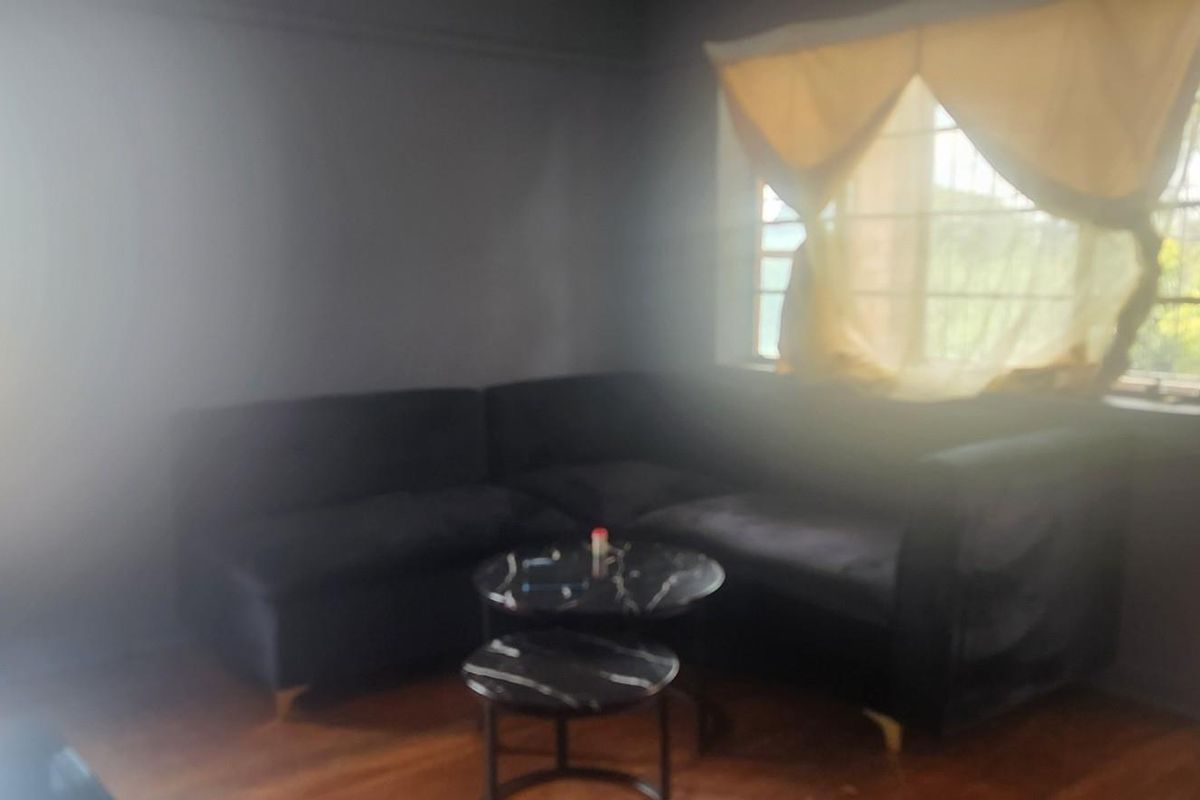 A living room featuring hardwood flooring and large windows with security bars, offering natural light.