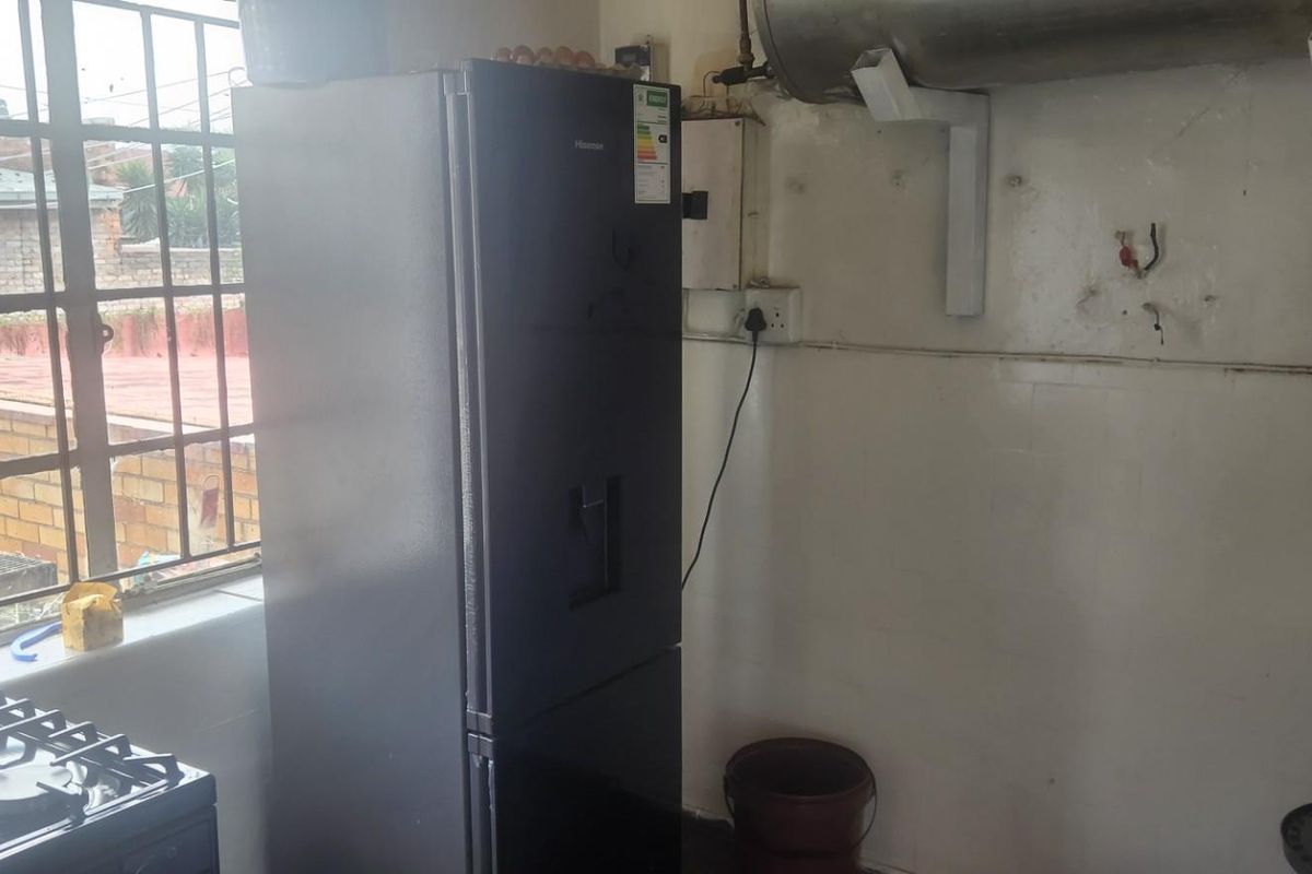 A functional kitchen area featuring a gas stove, wall-mounted water heater, and security-barred windows, requiring cosmetic updates and wall repairs.