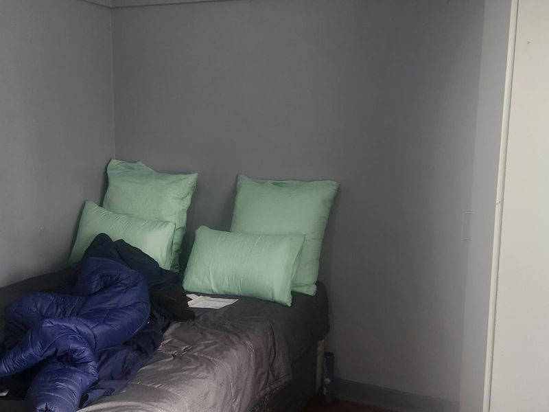 A compact bedroom featuring neutral grey walls and a built-in wardrobe, providing a functional sleeping space.