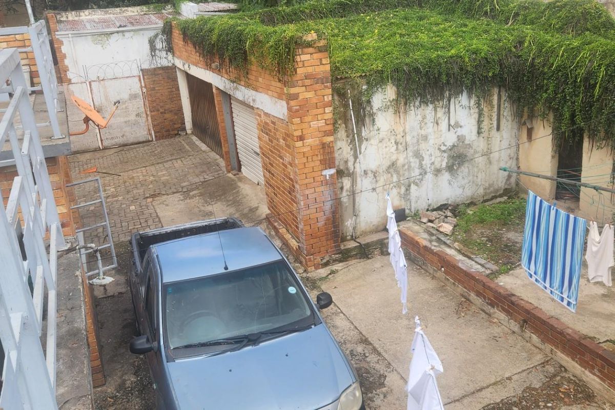 An elevated view of a rear courtyard area featuring a brick garage structure with significant weathering and overgrown vegetation on the roof.