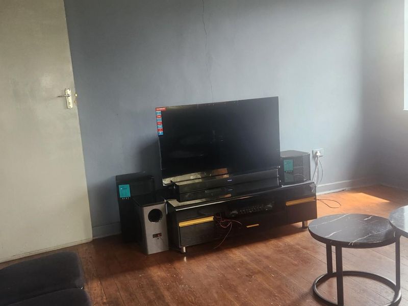 A living room featuring timber flooring and a window, showing signs of wear including a visible crack on the wall.