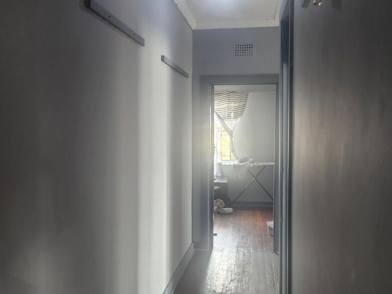 A narrow interior hallway featuring timber flooring and a ventilation grille, leading towards an adjacent room with natural light.