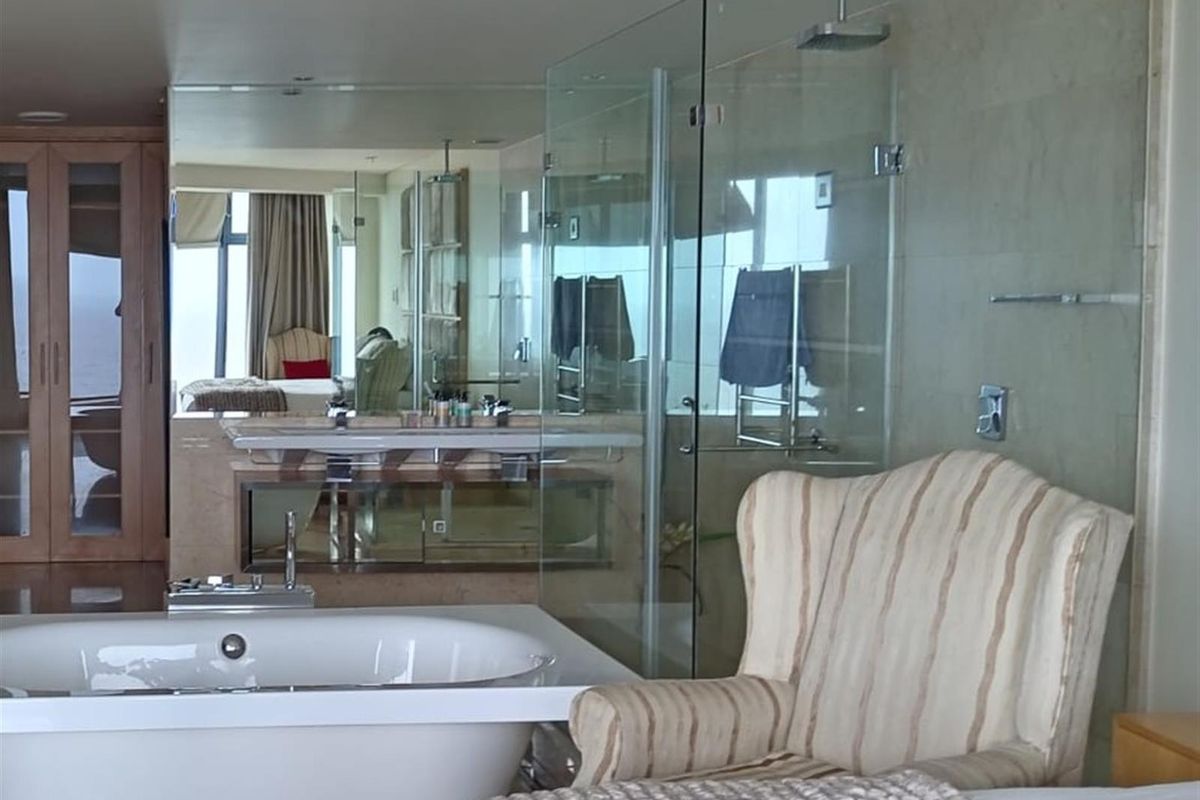 A spacious, modern bathroom featuring a freestanding bathtub, a glass-enclosed shower with a rain head, and a double vanity with extensive mirror work.