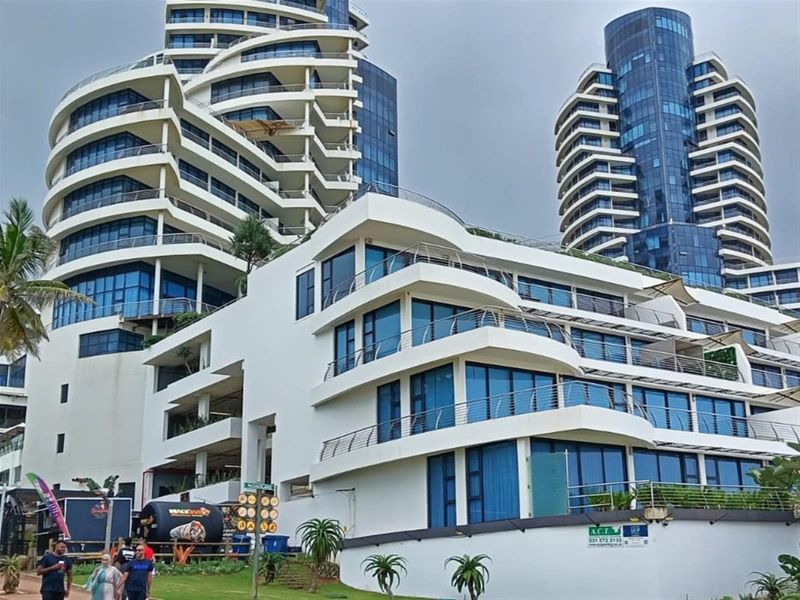 A modern multi-story apartment complex featuring contemporary architectural design, extensive glass facades, and private balconies with stainless steel railings.
