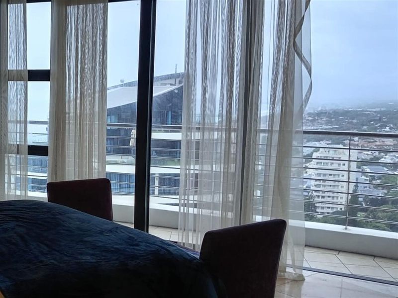 Bedroom featuring floor-to-ceiling sliding glass doors that open onto a private balcony with city views and stainless steel railings.