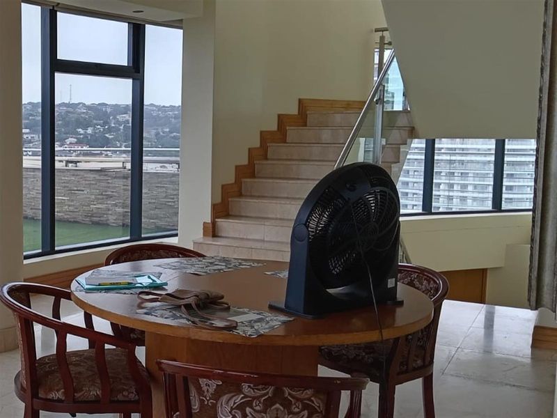 Spacious living area featuring a modern staircase with glass balustrade, large floor-to-ceiling windows, and tiled flooring with views of the surrounding area.