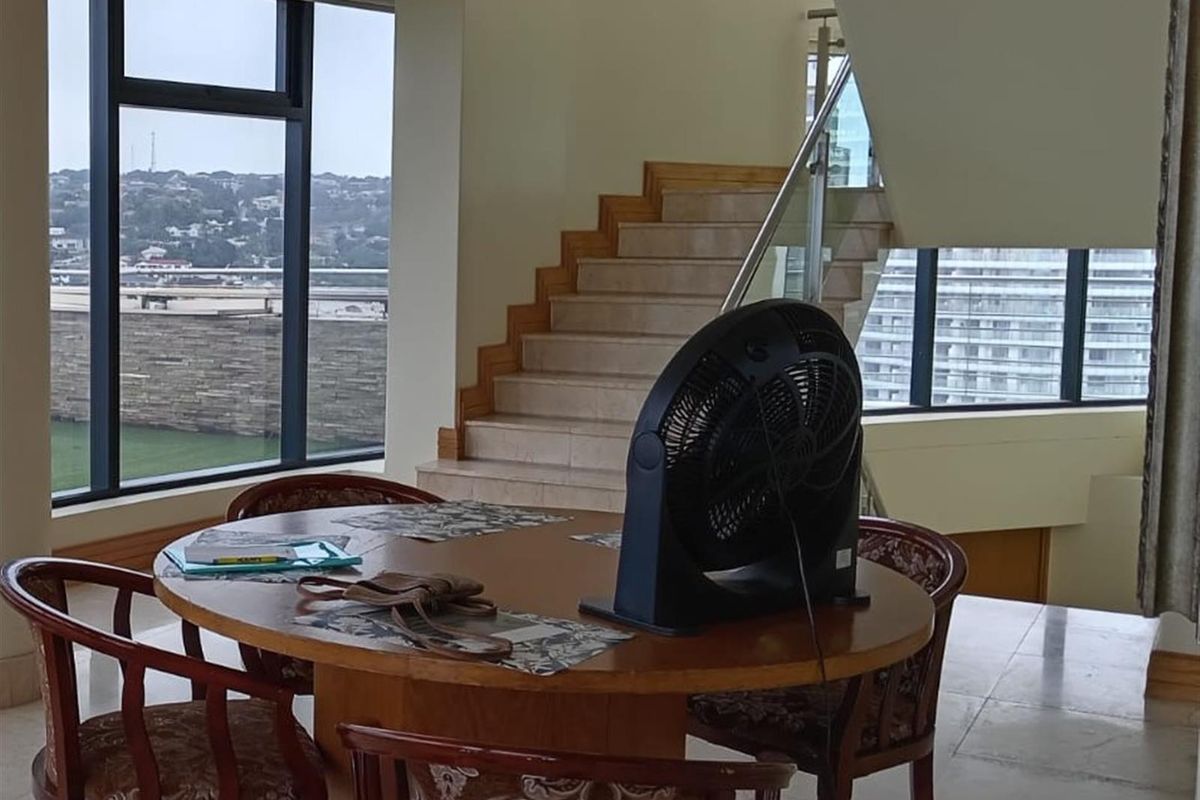 Spacious living area featuring a modern staircase with glass balustrade, large floor-to-ceiling windows, and tiled flooring with views of the surrounding area.