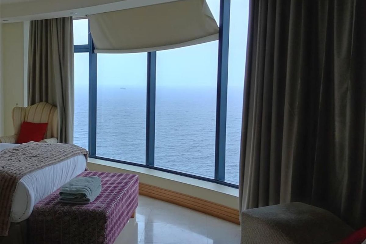 Spacious bedroom featuring floor-to-ceiling windows with expansive ocean views, tiled flooring, and neutral window treatments.