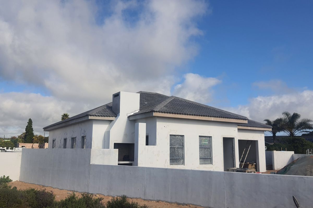 Rear view of a house under construction featuring a tiled roof, perimeter wall, and an integrated outdoor braai area.