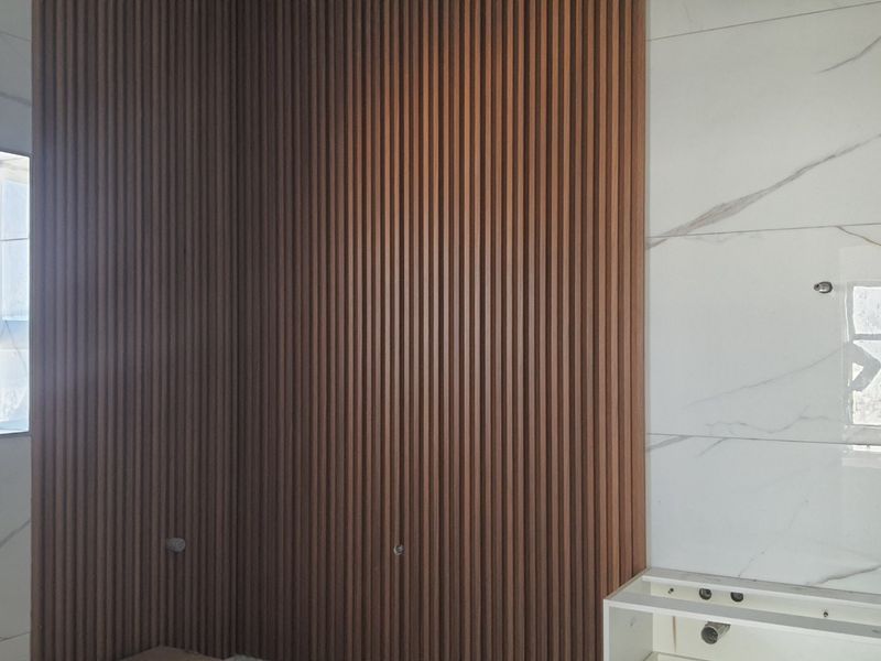 A bathroom under construction featuring modern slatted timber wall paneling and marble-look porcelain tiles, awaiting final vanity and fixture installation.