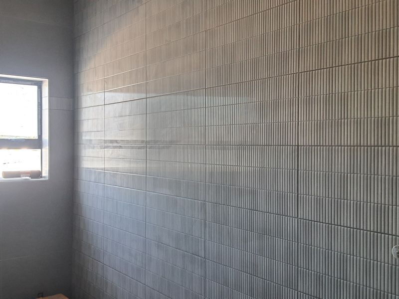 A modern bathroom space featuring contemporary textured wall tiling and a window, currently in a clean, unfinished state ready for final fixtures.